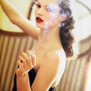 Kate Moss Smoking by Arthur Elgort, portrait of the model in a black off shoulder dress and vintage hairdo, holding a cigarette