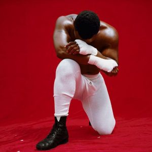 Mike Tyson by Michel Comte, the boxer in white pants and handwraps kneeling in front of red background