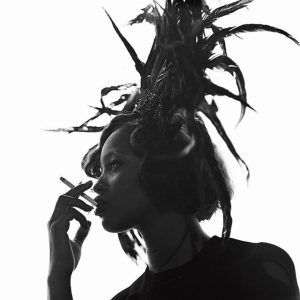Naomi Campbell by Michel Comte, black and white portrait of the model in sideprofile wearing a feather headpiece and smoking