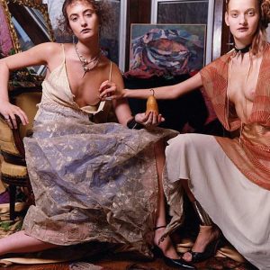 Grammercy Park 3 by Iris Brosch, two models in colorful dresses with exposed breasts sitting between paintings, one model pinching the nipple of the other