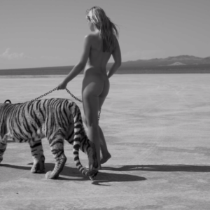 Tigress by Sylvie Blum, nude model walking through a desert, leading a tiger on a chian
