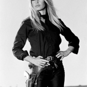 Brigitte Bardot standing by Terry O'Neill, the model in black with a holster and gun, standing with her hands on her hips and a cigarette