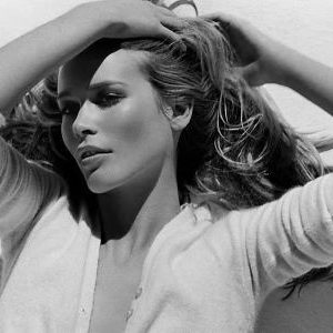 Claudia Schiffer Paris by bruno Bisang, black and white portrait of the model in a white cardigan, hands in her hair