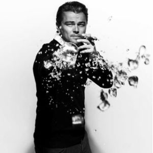 Leonardo DiCaprio Spilling his Drink by Nigel Parry, the actor in a black suit, smoking a cigarette and the drops of his drink spilling towards the camera