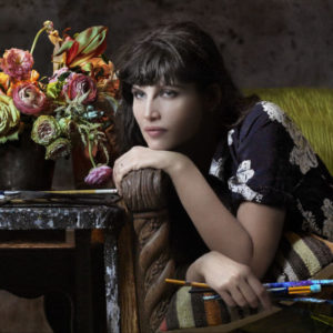 Laetitia Casta - Painter - Miami 2018-19 - Pirelli Calendar, the french actress lying on a sofa, holding brushes, next to a Bouquet