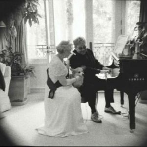 The real Elton John with the Queen by Alison Jackson, Elton playing the piano with the queen and a corgi sitting next to him