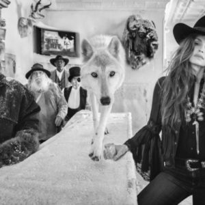 Hostiles by David Yarrow, white wolf standing on a bar and people standing around looking at the camera