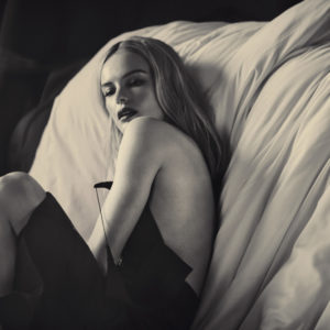 Kate Bosworth by Guy Aroch, black and white portrait of the actress in a black slipdress sitting next to a bed with white sheets