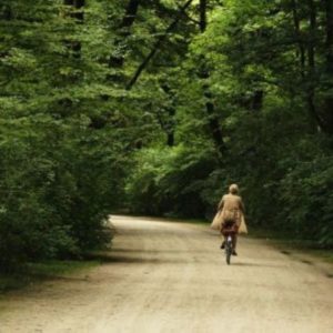 Germany by Marc Baptiste, person in a trenchcoat riding a bike through the forest