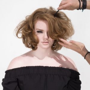 Shannon purser by Sylvie Blum, portrait of the actress in black off-shoulder shirt and messy hair, with two hands fixing her hair