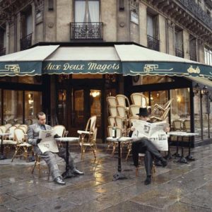 Elton John & Bernie Taupin Cafe in France by Terry O'Neill, the two me sitting in front of a cafe in the rain and reading newspapers