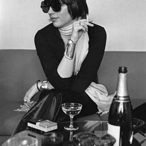 Liza Minnelli by Terry O'Neill, the singer sitting on a couch waerring sungalsses and smoking a cigarette, champagenglasses and bottle in front of her