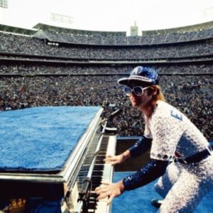 Elton John, Dodgers Stadium - Colour. 1975 by Terry O'Neill, the singer playing the piano in blue and yellow crystal suit