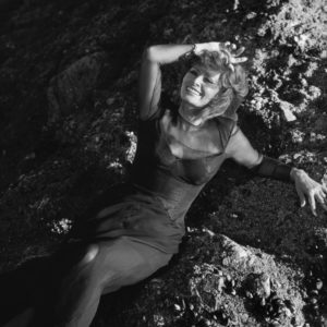 Sophia Loren by Timothy White, the actress i a sheer black dress posing on sunny rocks
