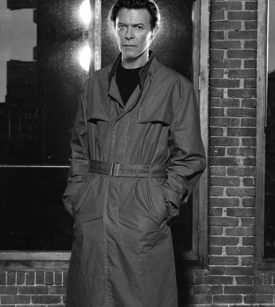 David Bowie New York by Markus Klinko, the singer in trenchcoat in front of window and brick wall