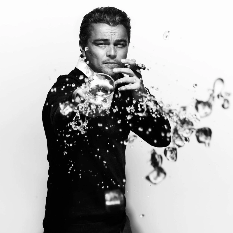 Leonardo DiCaprio Spilling his Drink by Nigel Parry, the actor in a black suit, smoking a cigarette and the drops of his drink spilling towards the camera