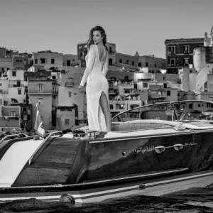 The Italian Job by David Yarrow - Model standing on a Motorboat infront of the italian Coastline with coastal village in the background
